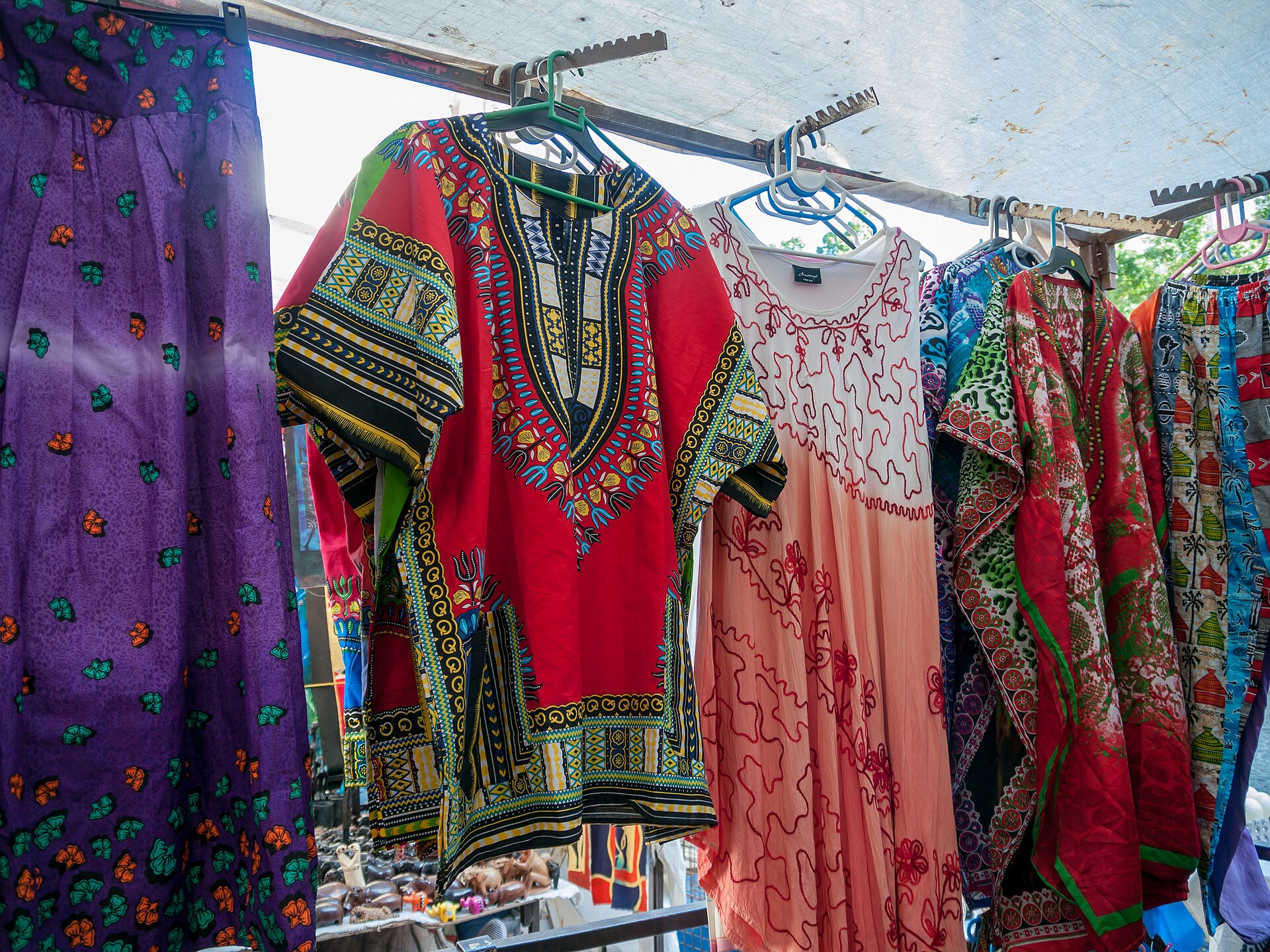 A market clothing stall under a white canopy, with a red and black patterned shirt and a purple dress on a rack.